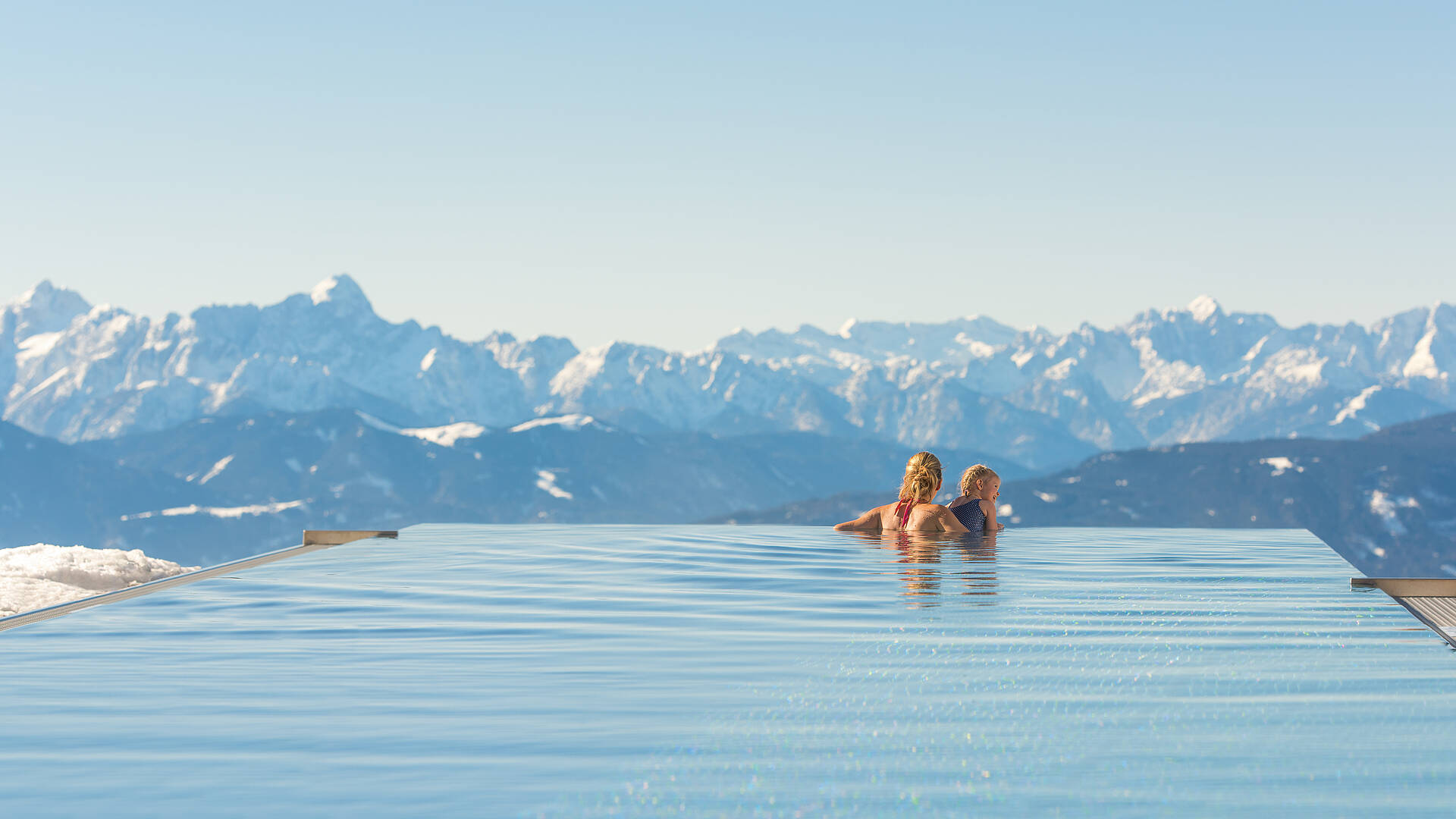 Mutter und Tocher im Pool betrachten die verschneite Winterlandschaft auf der Gerlitzen Alpe.