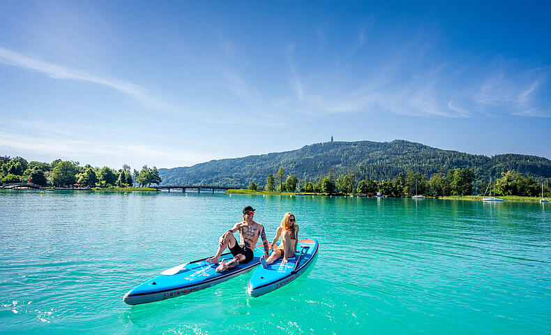 Mann und Frau sitzen am Stand Up Paddle und genießen einen schönen Sommertag am Wörthersee