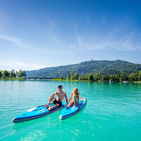 Mann und Frau sitzen am Stand Up Paddle und genießen einen schönen Sommertag am Wörthersee